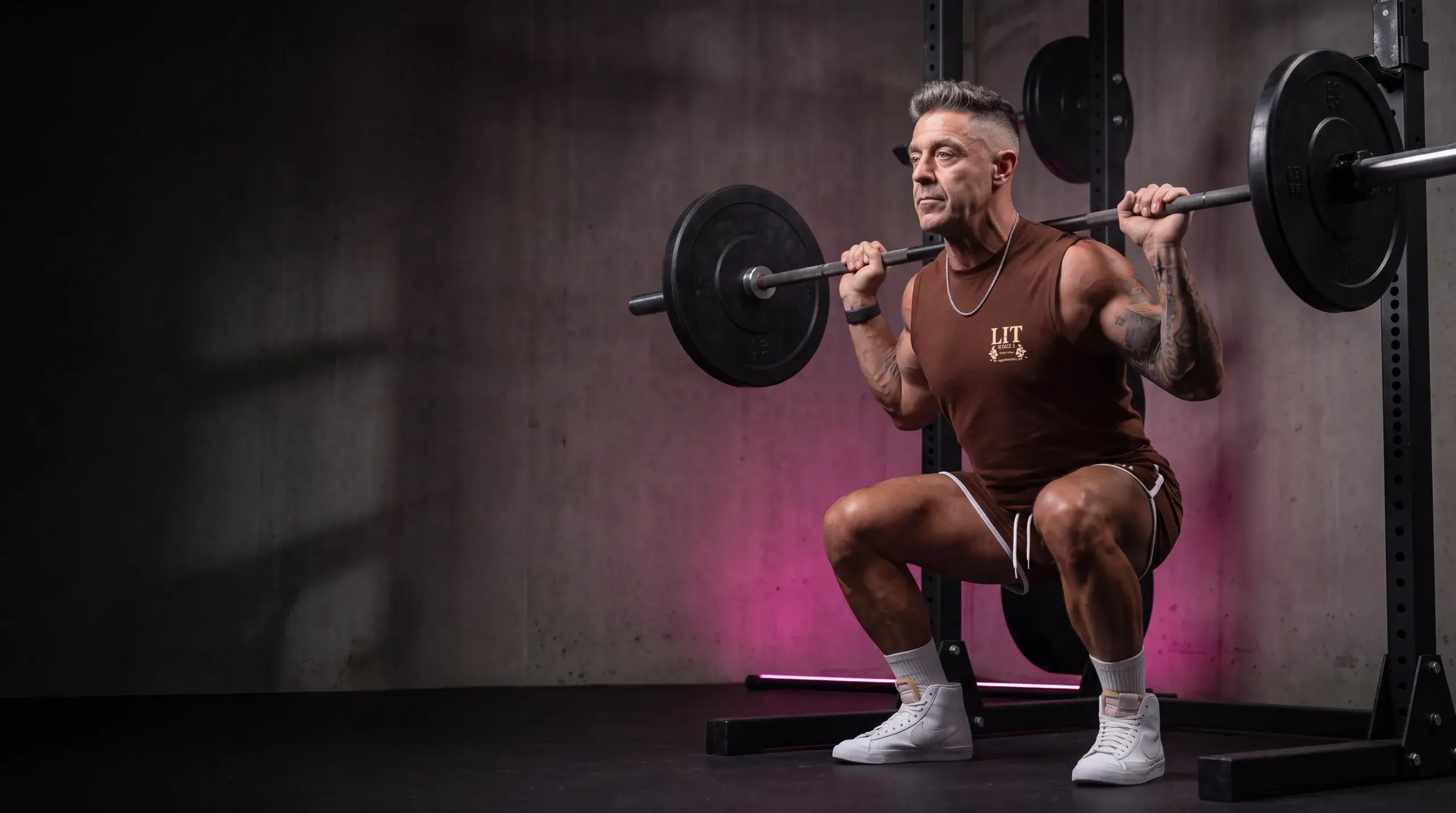 Kory at the bottom of a barbell back squat in a dark gym