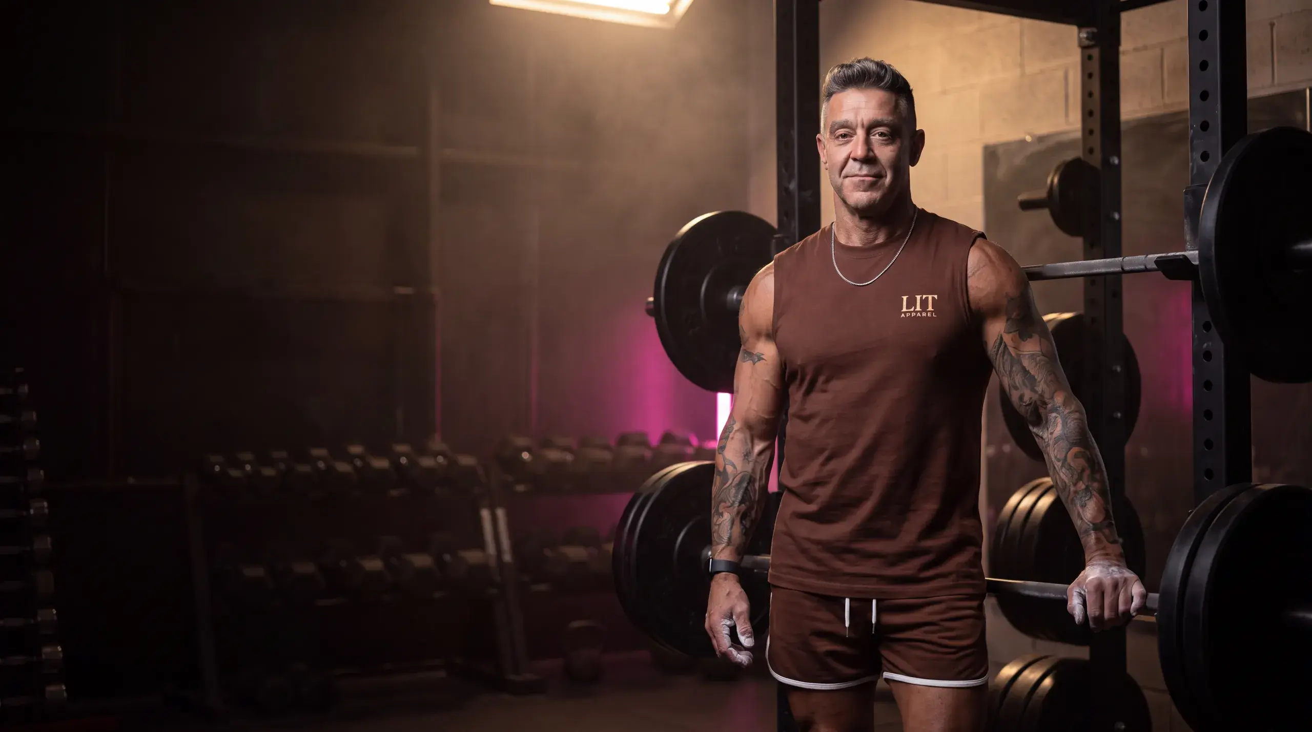 Kory, owner of Lit Apparel, beside a loaded squat rack in a gym