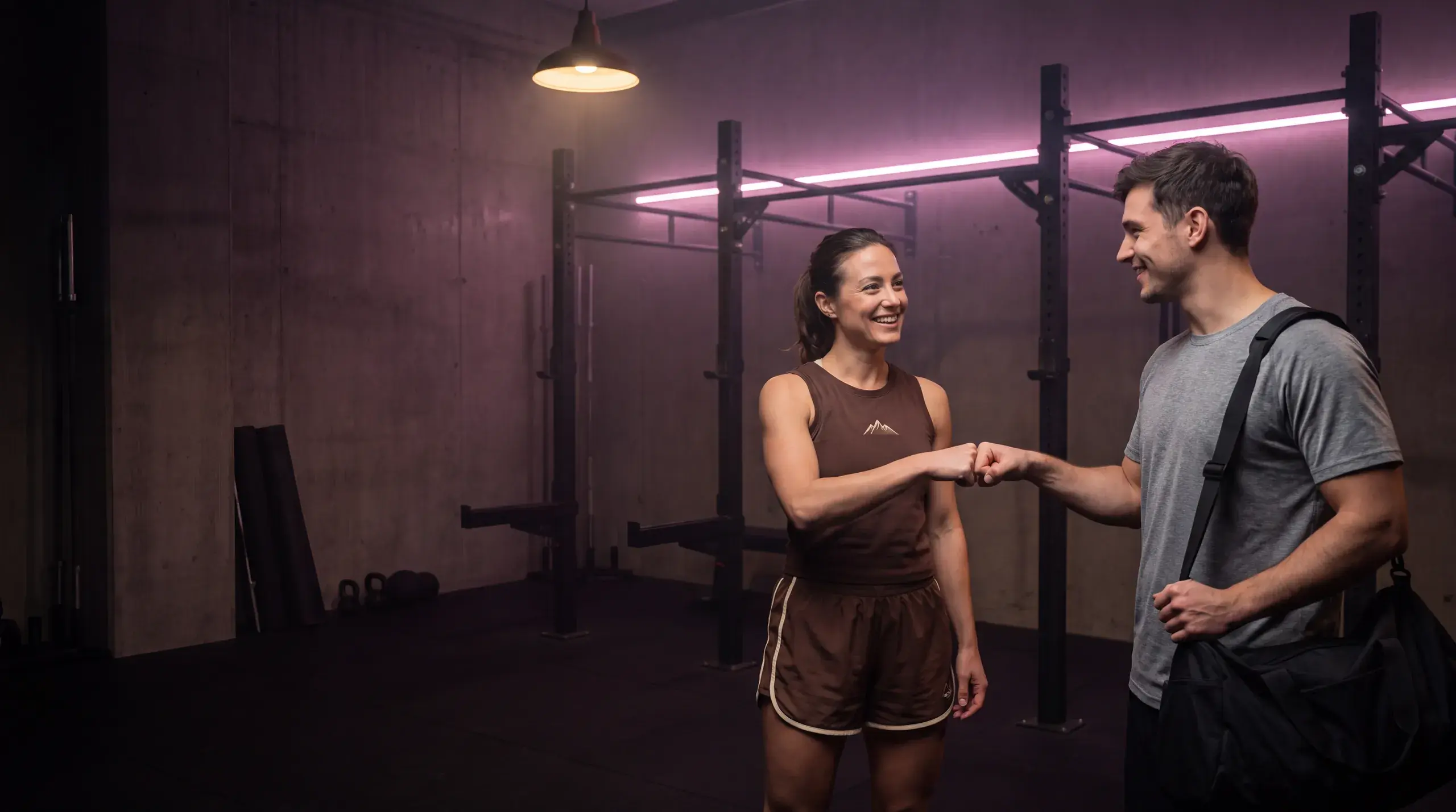 Two people meet with a fist bump on a gym floor lit with pink neon.