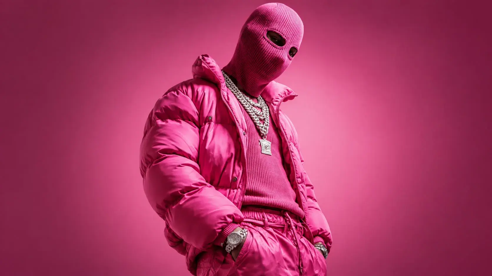 A model in a pink puffer jacket and pink balaclava against a flare-pink studio wall.