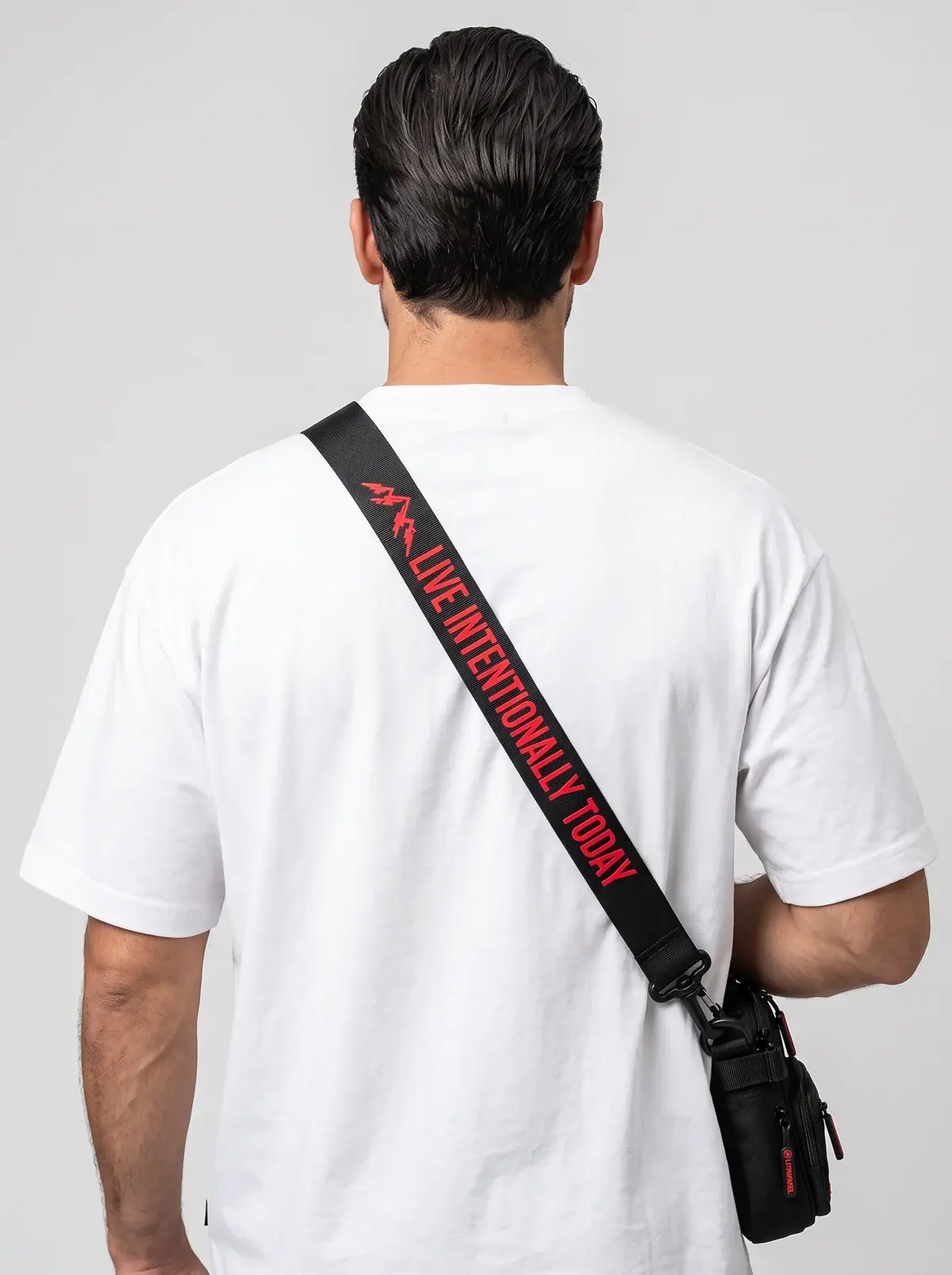 The back of a man in a white tee wearing the black LIT Tactical Sling, its strap printed with Live Intentionally Today in red.